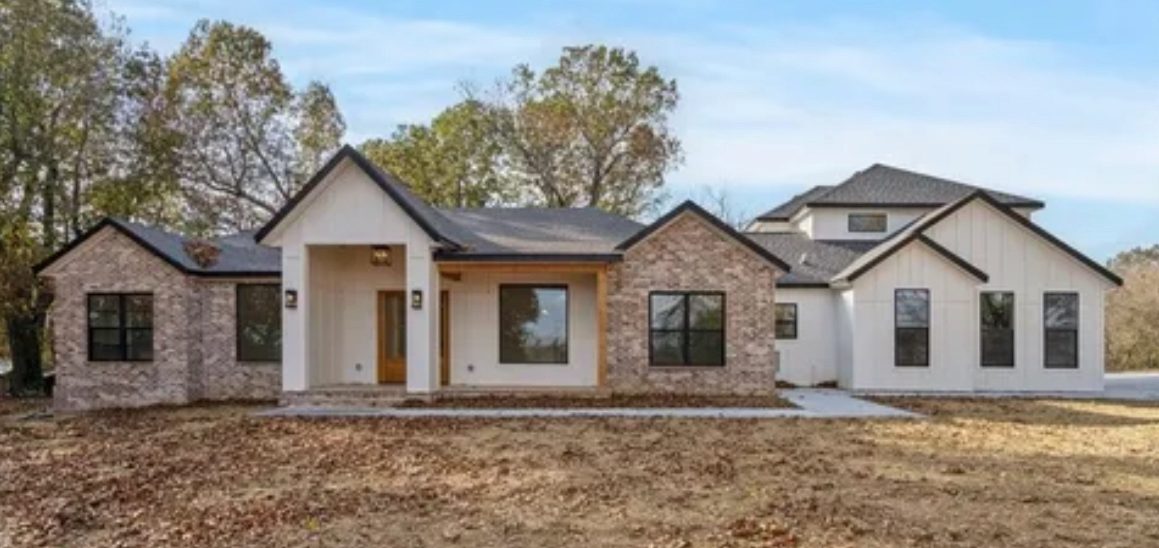 Arkansas New Build Modern two-story house with a mix of stone and white siding, surrounded by trees and grass.